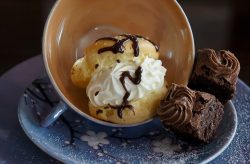 cream puff with chocolate syrup and brownie bites on a blue teacup