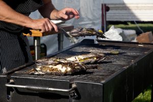 catering chef lifts fish off a grill at an outdoor catering event