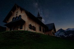 church on hill at night with stars snowy mountains in background